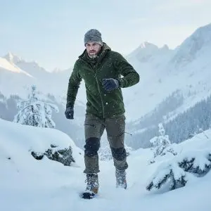 Homme en tenue de outdoor en hiver, veste verte, pantalon et bottes sur terrain enneigé avec montagnes en arrière-plan. Homme en tenue de outdoor en hiver, veste verte, pantalon et bottes sur terrain enneigé avec montagnes en arrière-plan.